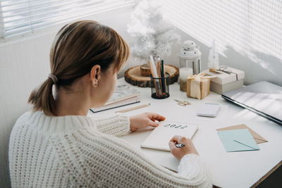 2022 goals, new year resolution. woman in white sweater writing text 2022 in open notepad on the