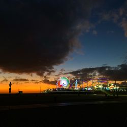 Illuminated ferris wheel at beach against sky at night