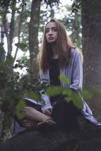 Young woman sitting on tree in forest