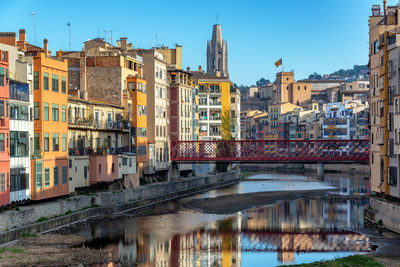 Bridge over river by buildings against clear sky