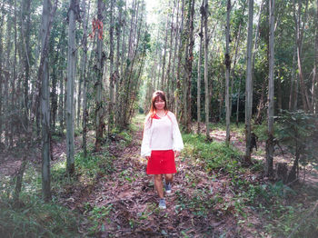 Full length of mid adult woman walking on field amidst trees in forest