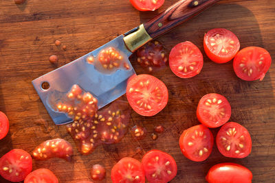 Overhead view flat lay of cut halves of grape tomatoes on wood cutting board with small cleaver