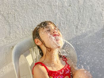Water splashing on mouth of girl against white wall