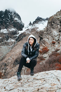 Full length of woman looking away while crouching on rock