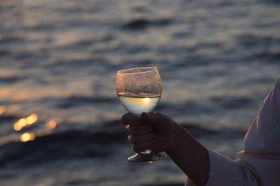 Close-up of hand holding wineglass against sky