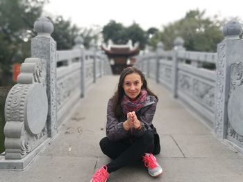 Portrait of smiling young woman sitting on footbridge