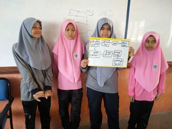 Girl with friends holding chart in classroom at school