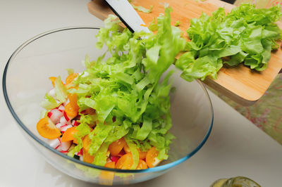 Salad with greens, tomatoes and radishes in a glass bowl. sliced lettuce on a board with a knife