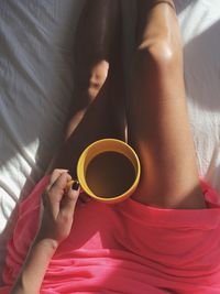 Low section of woman drinking coffee cup on bed at home