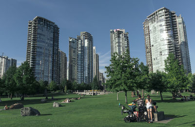 People in park by modern buildings against sky