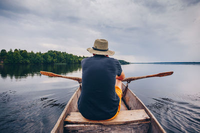 Rear view of man sitting on boat against sky