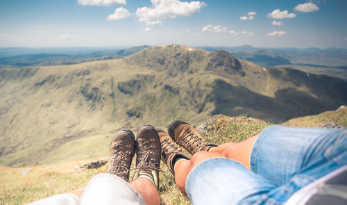 Low section of people relaxing on mountain against sky