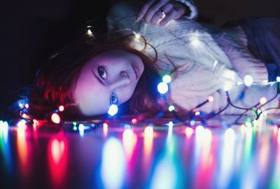 Portrait of young woman lying by illuminated string lights