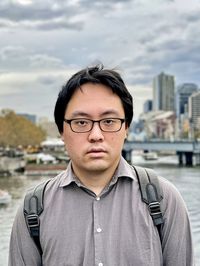 Portrait of young asian man in eyeglasses against river and buildings in the city.