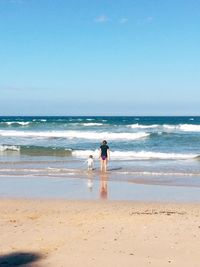 Rear view of father and daughter standing in sea against clear sky