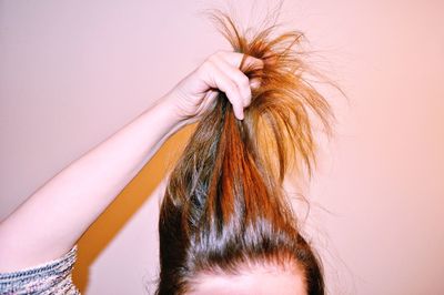 Cropped image of woman holding hair against colored background