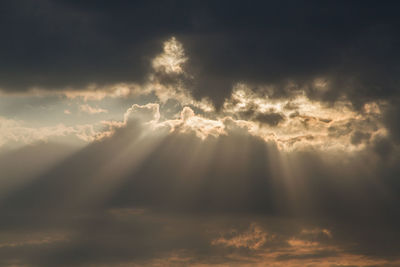 Low angle view of sunlight streaming through clouds