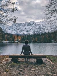 Rear view of woman sitting by lake against sky