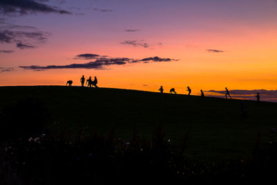 Silhouette people on hills during sunset