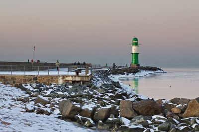 Lighthouse on pier at sea against sky in winter