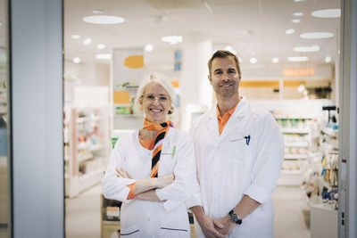 Portrait of confident mature owners standing at pharmacy store doorway