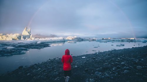 Rear view of woman by lake against cloudy sky during winter