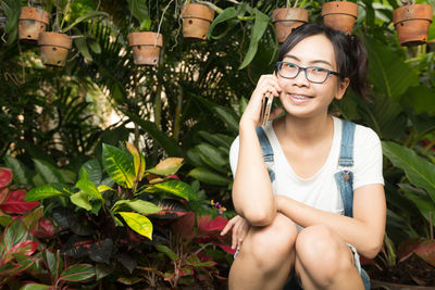 Portrait of smiling young woman talking on mobile phone against plants