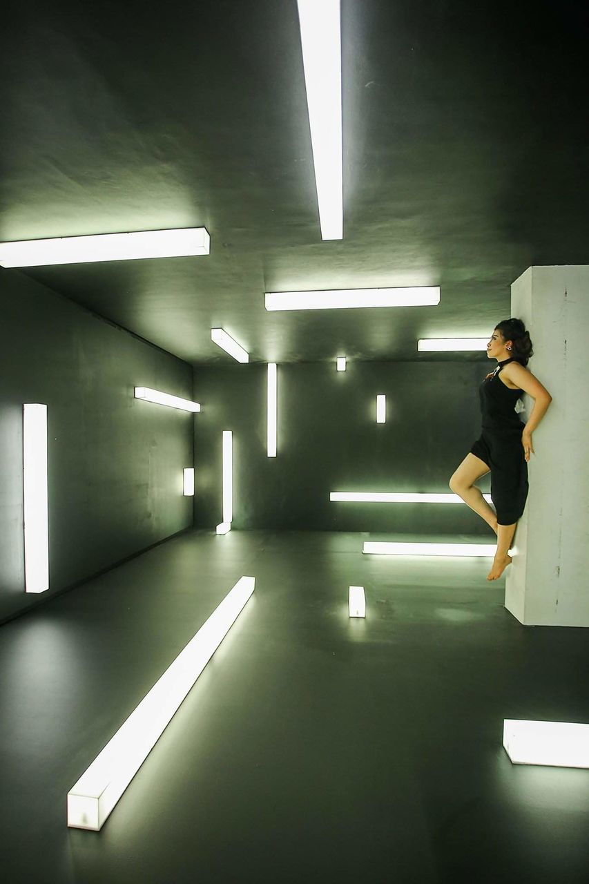 FULL LENGTH OF WOMAN STANDING AGAINST ILLUMINATED WALL IN CORRIDOR