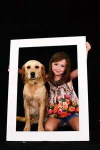 Portrait of smiling woman with dog against black background