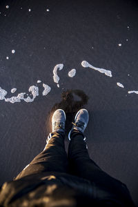 Low section of man standing on wet shore at beach