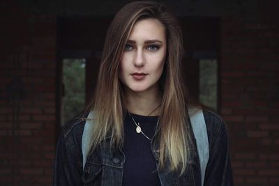 Portrait of beautiful young woman standing against brick wall