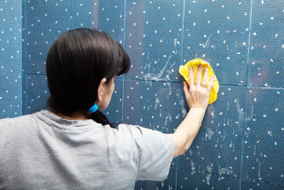 Woman cleaning tiled wall at home