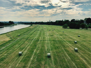 Scenic view of agricultural field with hay bales by a river and against sky