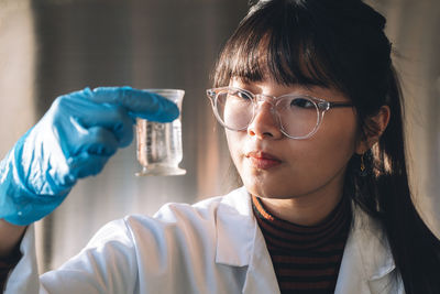 Young scientist wearing eyeglasses examining solution in glassware