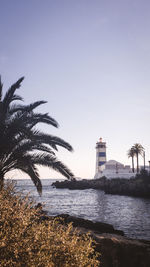 Lighthouse by sea against clear sky