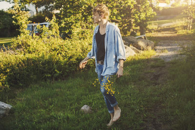 Full length of young man holding flowers while walking on grass
