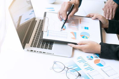 Midsection of businesswoman and colleague discussing over graph at desk in office