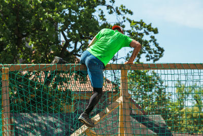 Side view of man standing by fence against trees