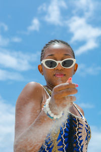 Portrait of woman wearing sunglasses playing with sand against sky