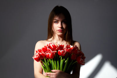 Portrait of young woman holding bouquet against black background