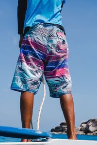 Low section of man standing on boat in sea against clear blue sky