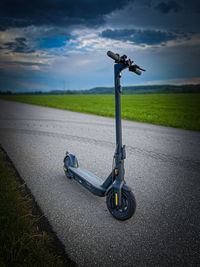 Bicycle on road amidst field against sky