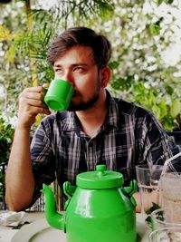 Young man looking away while having drink at table