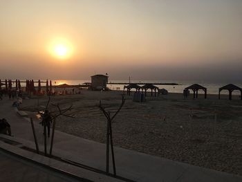 People on beach by road against sky during sunset