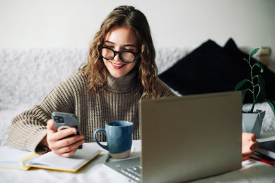 Smm specialist working from home at kitchen table, using smartphone to select blogger for product