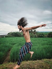 Man with arms raised on field against sky