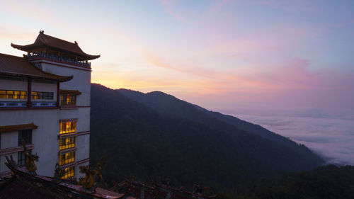 Scenic view of building by mountains against sky during sunset