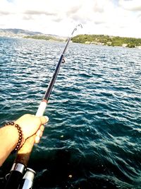 Person holding fishing rod by sea