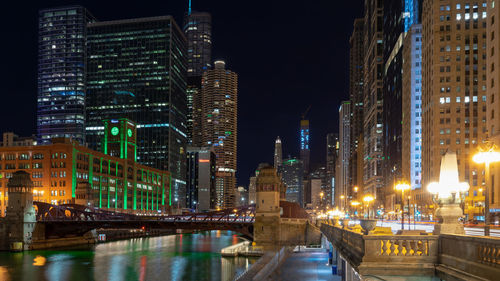 Illuminated buildings by river in city at night