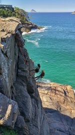 High angle view of people rock climbing against sea